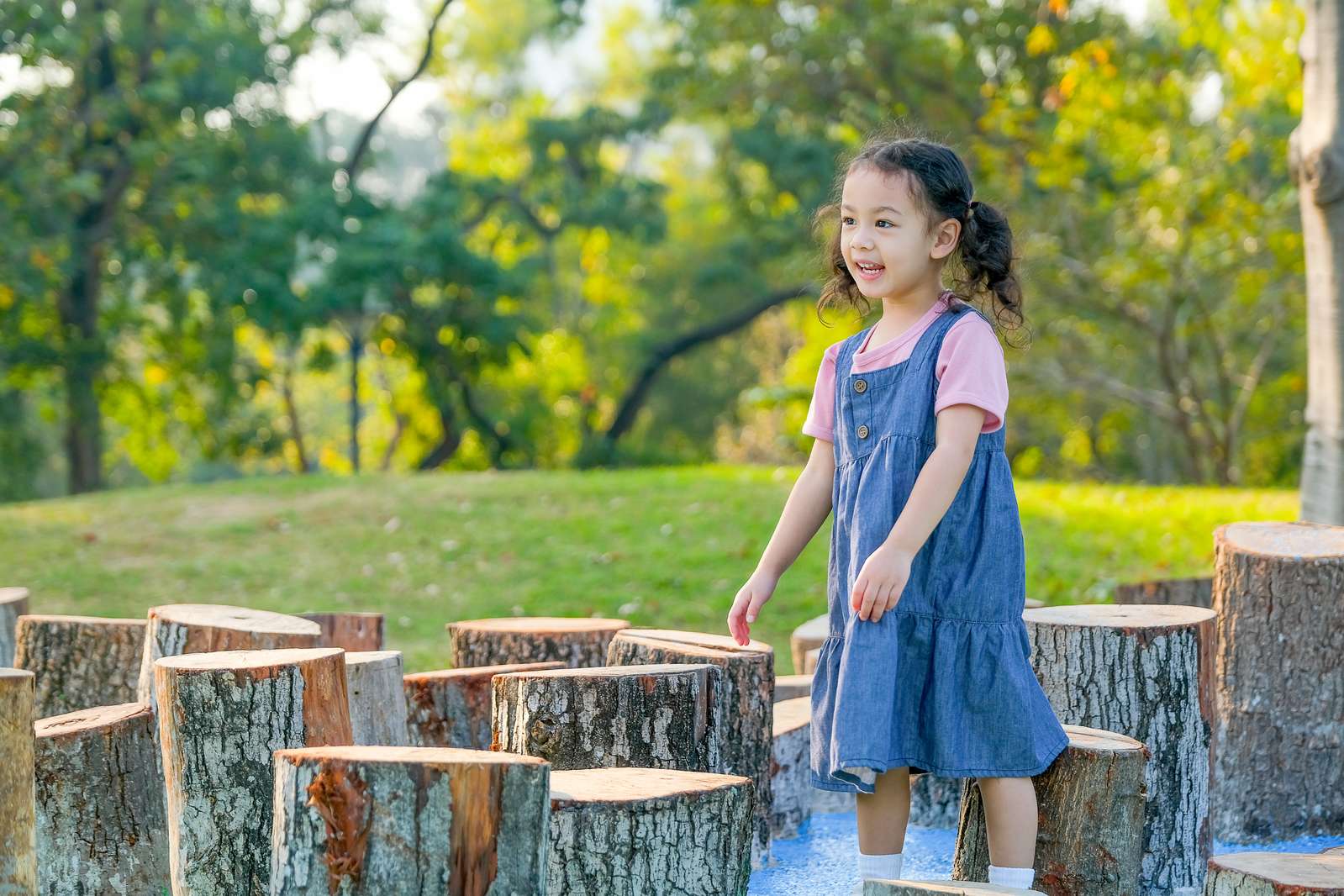 Child playing among natural tree-stump stepping features in a garden play area
