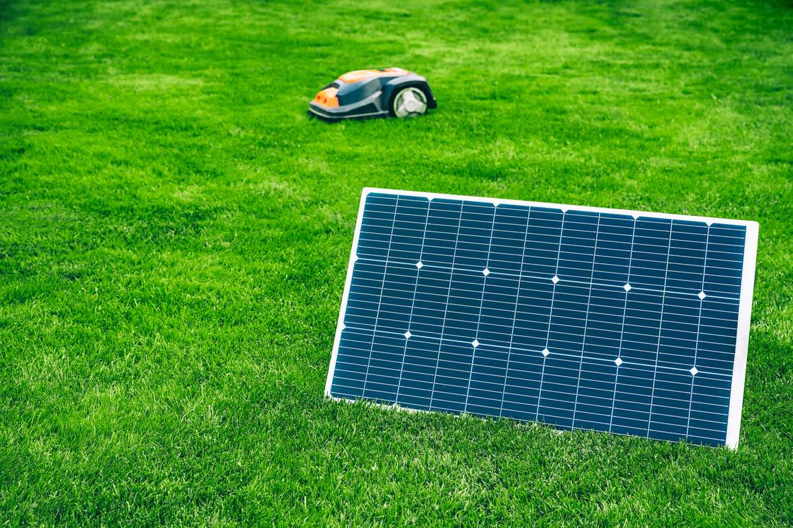 Solar-powered robotic mower operating on a lawn next to its charging panel